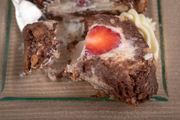 Chocolate roulade filled with cream and strawberries. Decorated with whipped cream. It lies on a glass tray ready for portioning and eating.
