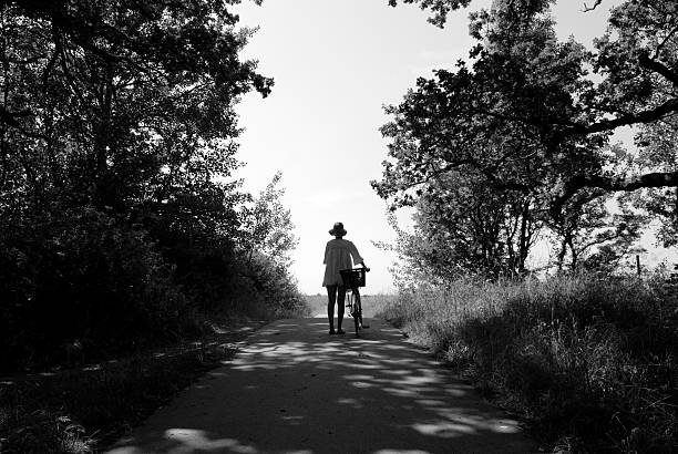 Woman standing with her bicycle by the edge of a forest looking towards the horizon by the sea.