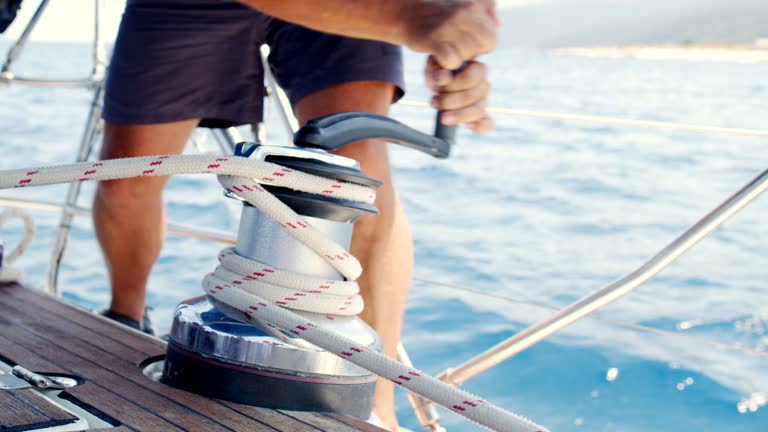 Man pulling rope on sailboat and using winch