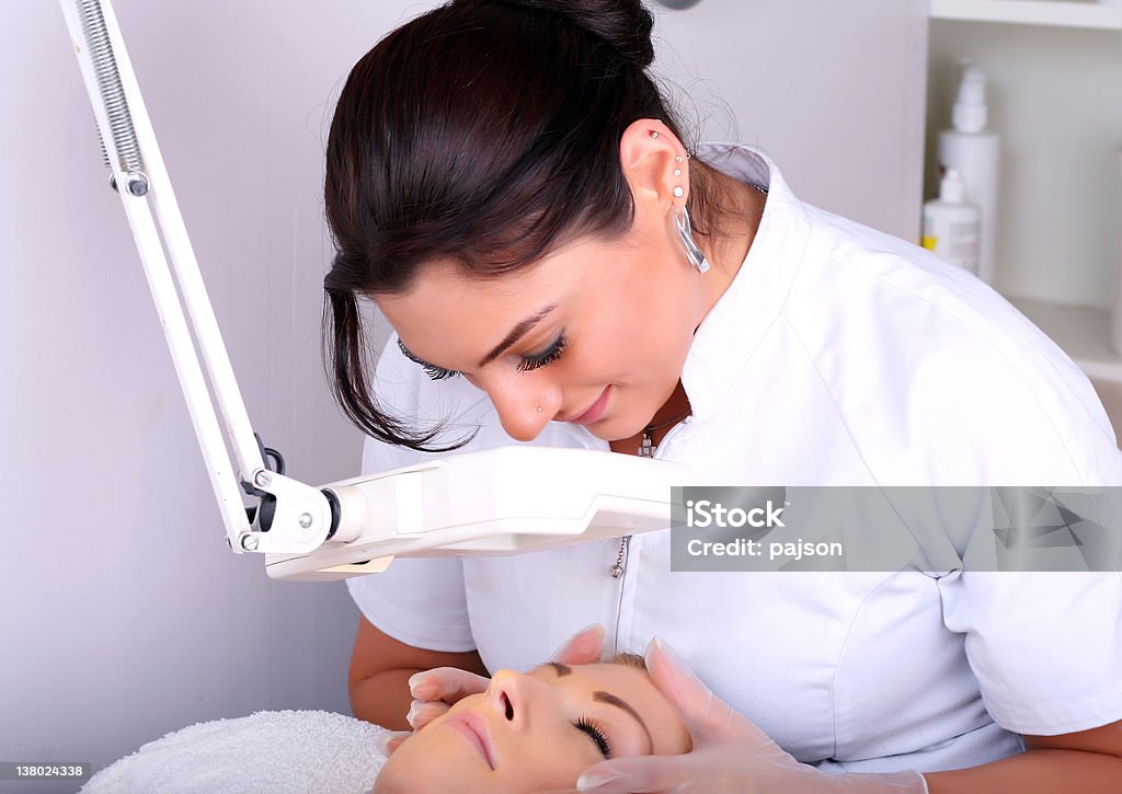 A health care professional examines a patient's face Skin treatment in a beauty salon Activity Stock Photo