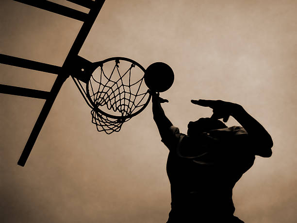 Looking up at a man jumping up to put basketball in a net