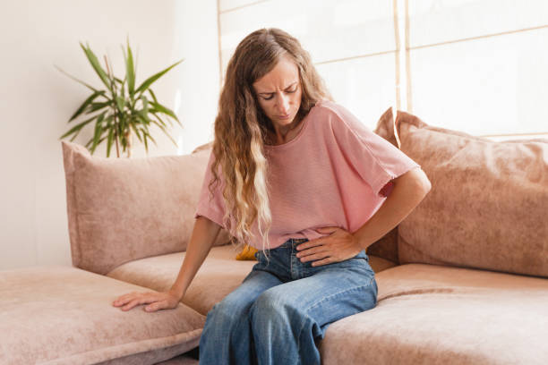 istock Young woman suffering from strong abdominal pain while sitting on sofa at home 1380289891