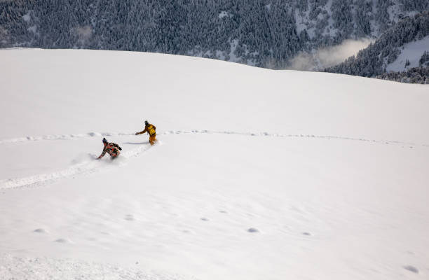 istock Two snowboarders riding down in a deep powder snow during a winter vacation 1380307365