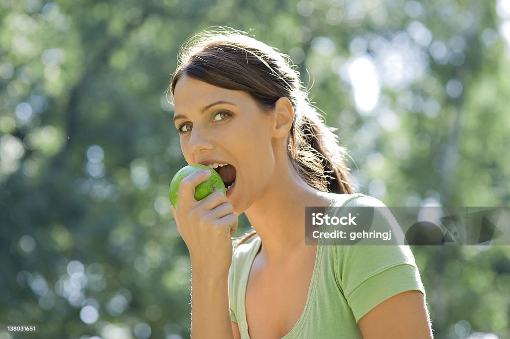 Beautiful young woman eating apple in the park Apple - Fruit Stock Photo