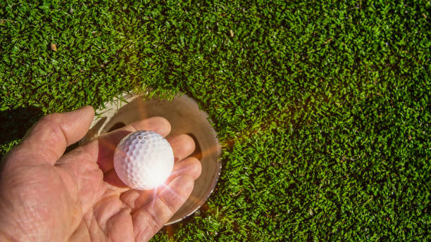 istock Hand with golf ball near hole with artificial sun rays 1380317474