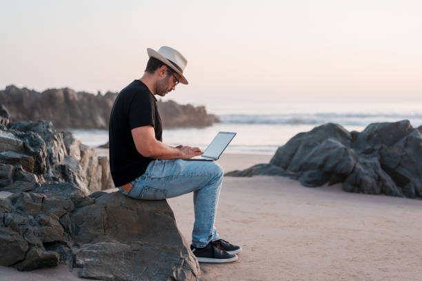 istock man sitting on the beach with a laptop alone doing telecommuting or remote work 1380329228