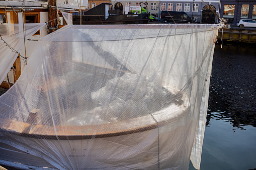 Old fishing vessel made of wood under a tarpaulin during repair in Nyhavn - New Harbor in the middle of Copenhagen. New Harbor is despite the name the oldest part of Copenhagen harbor and is today a kind of working museum for wooden ships