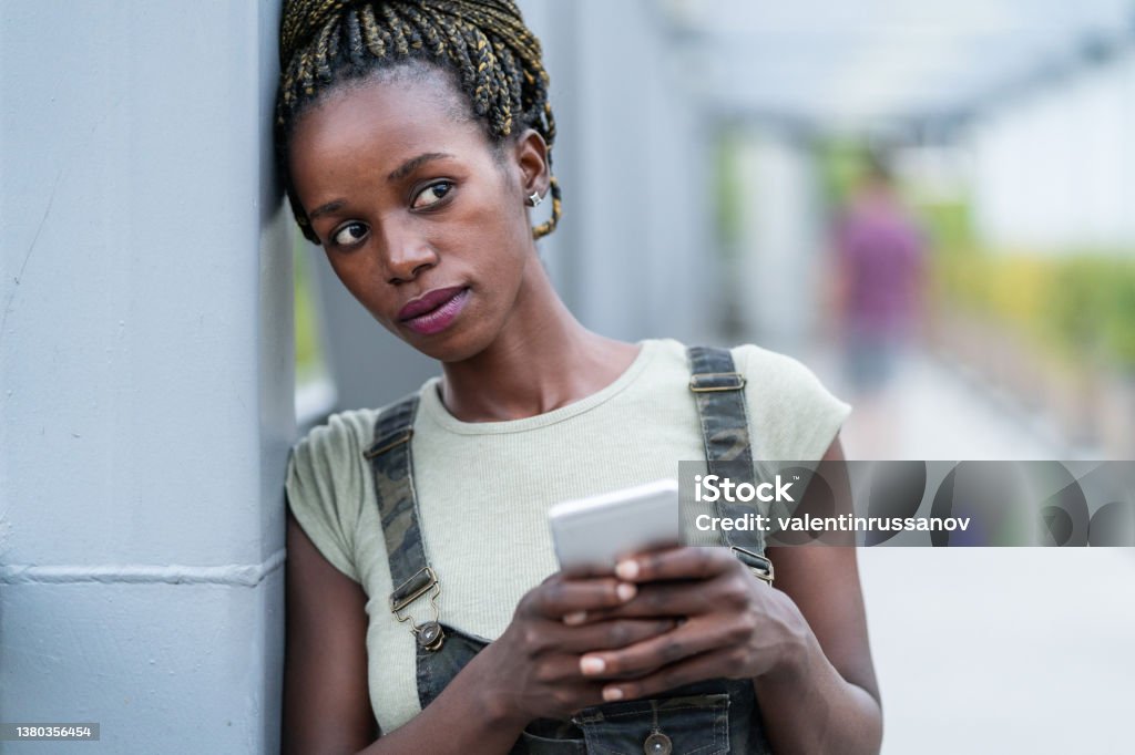 Close up of an young african woman with mobile phone,  standing on a iron bridge depression Close up of an young african woman with mobile phone,  standing on a iron bridge African Ethnicity Stock Photo