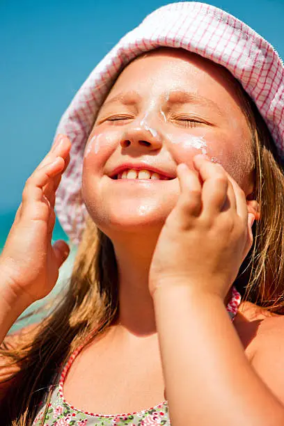 Little girl applying sun-protection lotion on the beach