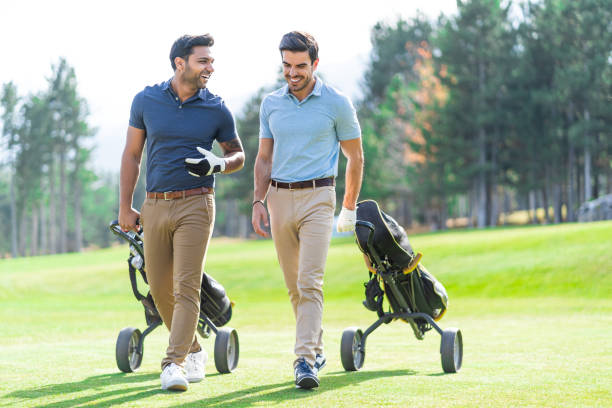istock Smiling young golf players holding golf clubs and pulling their wheeled golf bags while talking on a golf course. 1380360309
