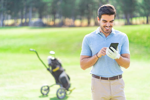 골프 클럽과 그의 가방 옆에 서 코스에 자신의 휴대 전화에 이야기 웃는 골프 선수 - beautiful golf course relaxation happiness 뉴스 사진 이미지