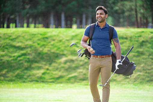 Indian ethnicity smiling golf player walking on the course and carrying his golf clubs