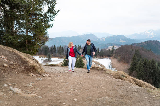 Happy adult couple walking or jumping up the hill and holding hands.