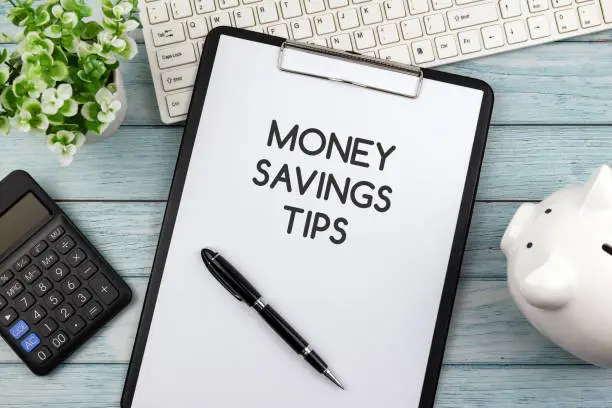 Money savings tips text on clipboard, piggy bank, calculator and computer keyboard