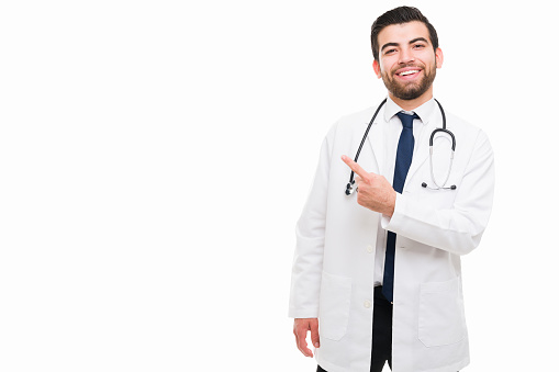 This is the best medical practice. Handsome happy doctor pointing next to copy space in front of a white background