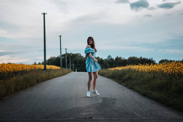 Young 20-24 year old slim brunette in a light blue summer dress dances on the road to the rhythm of the music. Candid portrait of a real ordinary person enjoying movement and dancing. Knowing oneself stock photo