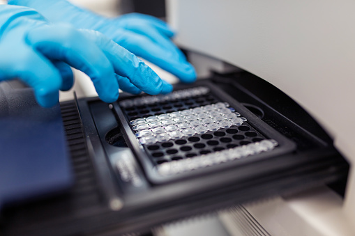 scientist putting test 96 well plate into real-time PCR machine