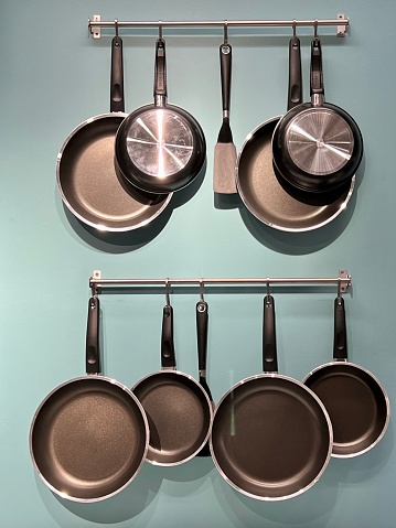 Set of kitchen metallic pans hanging on a pot rack in the kitchen