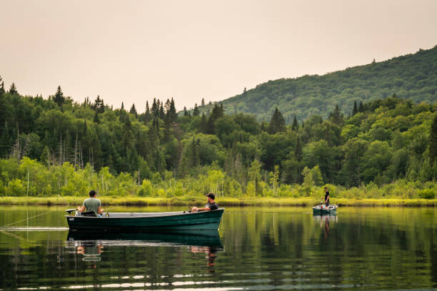 Three men fishing on a lake during a cloudy sunset of summer in Quebec.