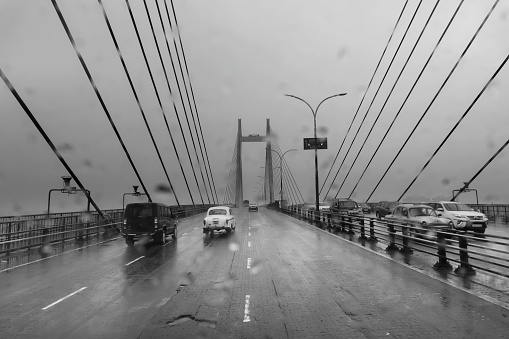 Howrah, West Bengal, India - 17th August 2019 : Image shot through raindrops falling on car windshield , wet glass, traffic at 2nd Hoogly bridge. Monsoon stock image. Black and white.