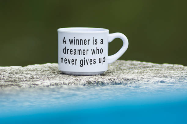 Motivational quote on coffee cup with blue water background - A winner is a dreamer who never gives up