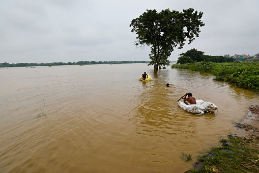 Katwa WB India - August 9, 2021 : Taken this picture during the flood in West Bengal where villagers are crossing the inundated countryside on boat. Few people are fishing and few crossing the street carrying belongings. Kids playing using makeshift raft.