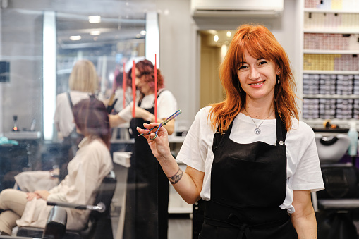 Hairdresser holding a scissor in her hand while standing in the hair beauty salon. Hair care and styling concept.