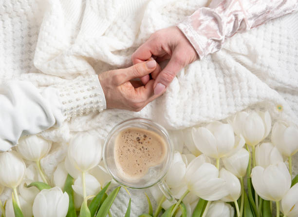 hands of two women holding a heart-shaped cup with cappuccino on two sides, female friendship, hands of two women holding a heart-shaped cup with cappuccino on two sides, female friendship, flat lay with white tulips, mother's day, valentine's day, cup shaped flower stock pictures, royalty-free photos & images