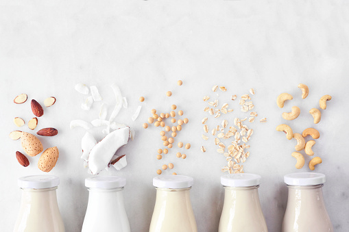 Vegan, plant based, non dairy milk. Variety in milk bottles with ingredients. Above view over a white marble background.