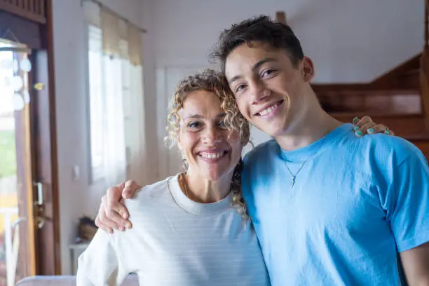 Photo of Portrait of grateful teenager man hug smiling middle-aged mother show love and care, thankful happy grown-up son in embrace cheerful mom, enjoy weekend family time at home together, bonding concept