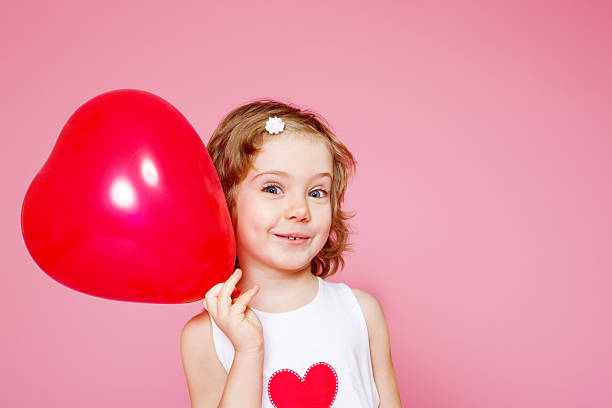Portrait of a cute smiling preschool girl with a red balloon, over pink