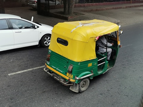 New Delhi, India- August 3, 2019- A taxi driver, driving an auto rickshaw or tuk tuk in New Delhi, India. Green and yellow tuk tuks are iconic scenes in India.