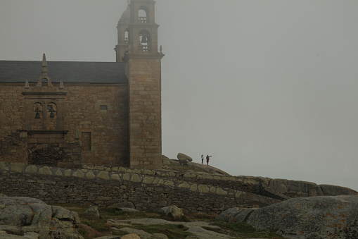 2018 June 24. Spain. Muxía. People take selfies in front of Santuario da Virxe da Barca, on the rocks of Costa da Morte