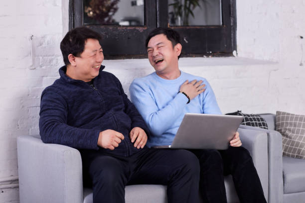 istock Two East Asian men sat on the sofa and laughed loudly. They couldn't stop interesting positive emotions in the conversation. Happy friends sat with laptops and laughed happily 1380580151