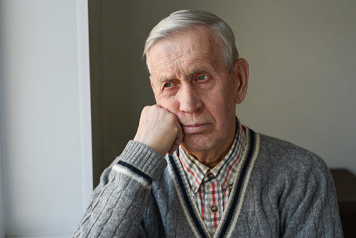 A handsome elderly man is sad, pensive, looking out the window.
