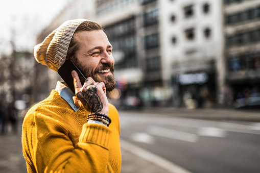 Cheerful tattooed hipster man having a phone conversation in the city.