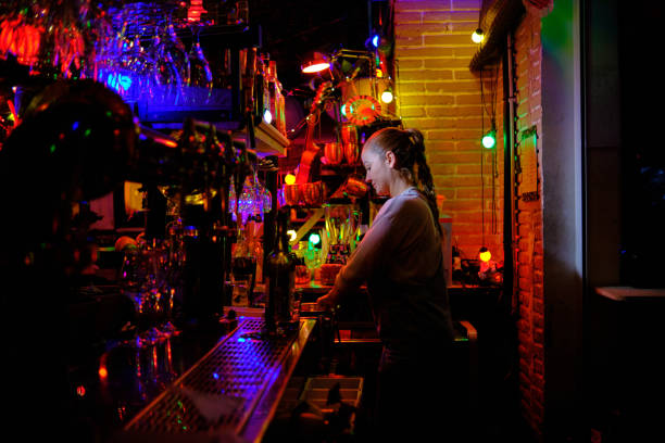 istock Female bartender standing behind the counter preparing an order for a customer while working in a bar or pub. 1380617813