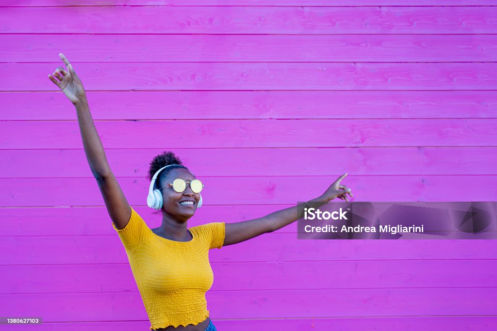 African girl dancing alone, with headphones on her ears, listen to music in a silent disc, sense of freedom and joy, contrast of yellow and pink color Generation Z Stock Photo