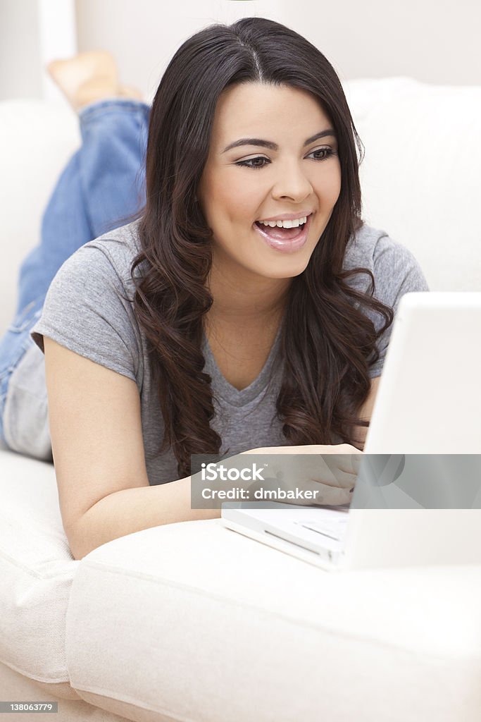 Happy Hispanic Woman Using Laptop Computer Beautiful happy young Latina Hispanic woman smiling and using a laptop computer at home on her sofa Adult Stock Photo