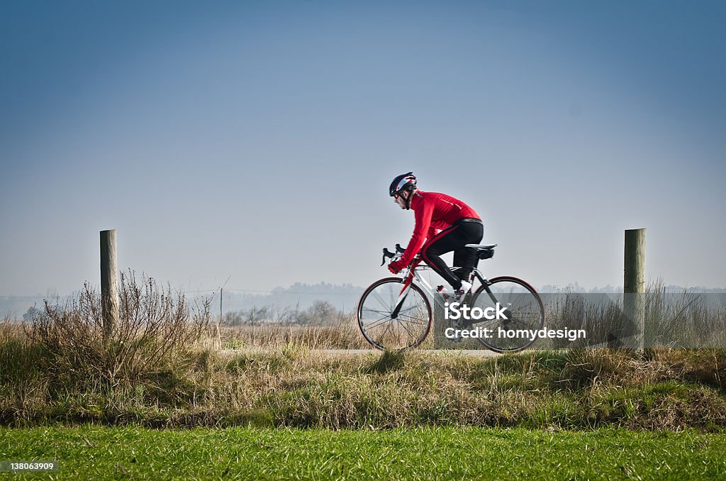 Cyclist in red on a rural bike path Man on road bike riding down open country road. Adult Stock Photo
