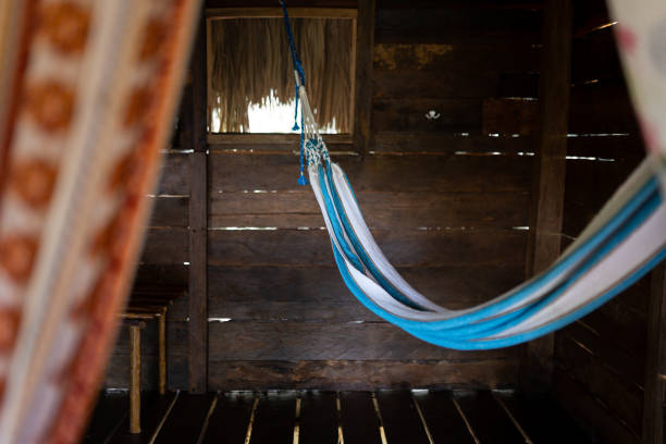 A blue hammock is hanging inside of a wood cabin with a palm roof. Concept of relaxing retreat.