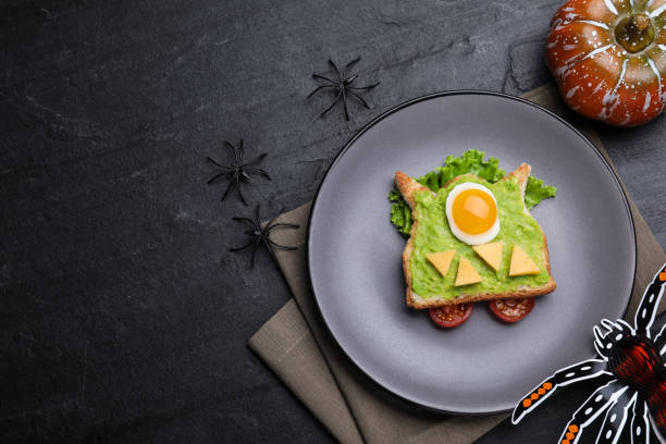 Halloween themed breakfast served on black table, flat lay and space for text. Tasty sandwich with fried egg