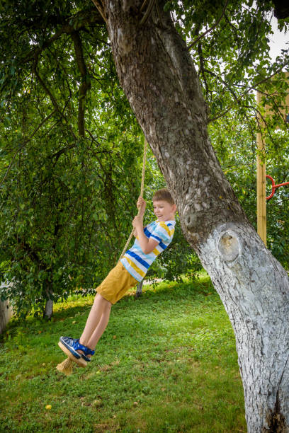 istock Happy little boy is having fun on a rope swing which he has found while having rest outside city. Active leisure time with children 1380703744