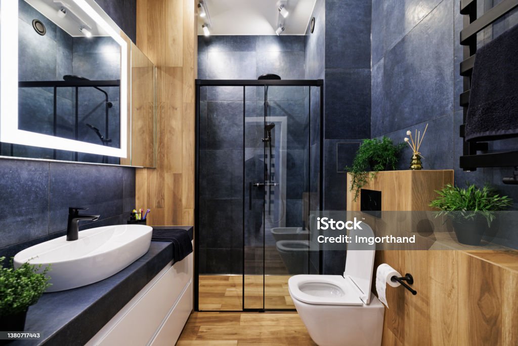 Dark blue modern luxury bathroom. Modern, dark luxury bathroom with indigo and wood like tiles. Black rain shower head. Lacquered white drawers. Modern mirror with built-in led illumination.
Canon R5. Bathroom Stock Photo