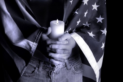 American Flag draped around male figure holding a lit candle