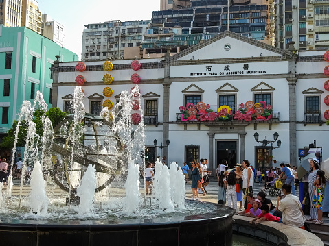 Macau, Island of Macau, China - September 15 2019: water fountain in the city. Traditional Portuguese architectute behind it, and a lot of tourists.
