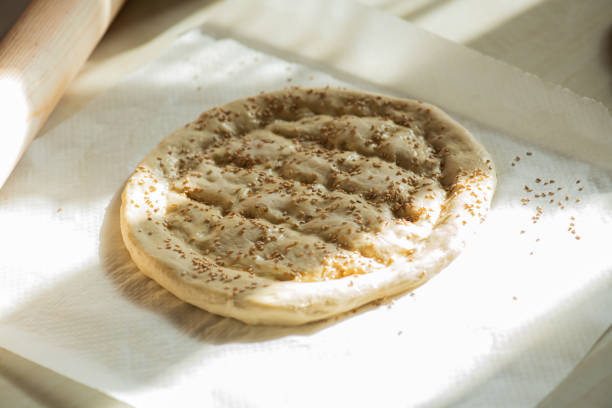 Round piece of dough on a table, preparing Ramadan pide with sesame seeds.