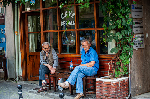 Two middle aged men sit together chit chatting outside of a cafe in Istanbul, Turkey.
