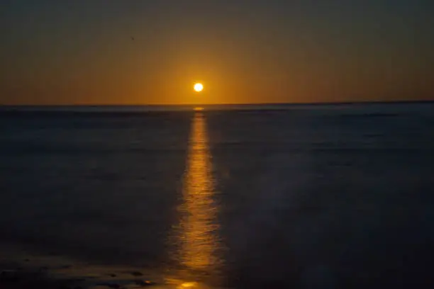 Sunrise just on horizon starts to illuminate and warm the air over sea through dawn darkness of Tokomaru Bay New Zealand.