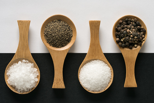 Sea Salt Flakes, Ground Black Pepper, Kosher Salt and Black Peppercorns on Wood Spoons